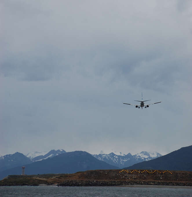 A plane landing over the water with mountains in the background.