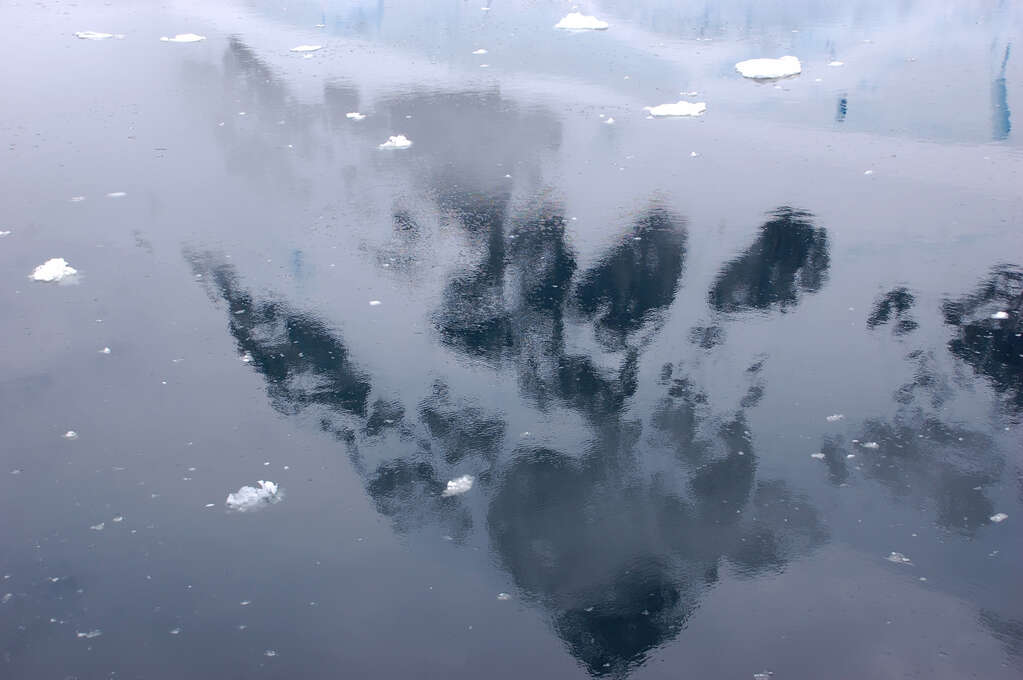 A snow-covered mountain reflected in very still water.