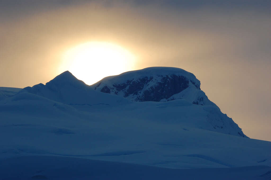 The sun starting to appear over a snow-covered ridge.