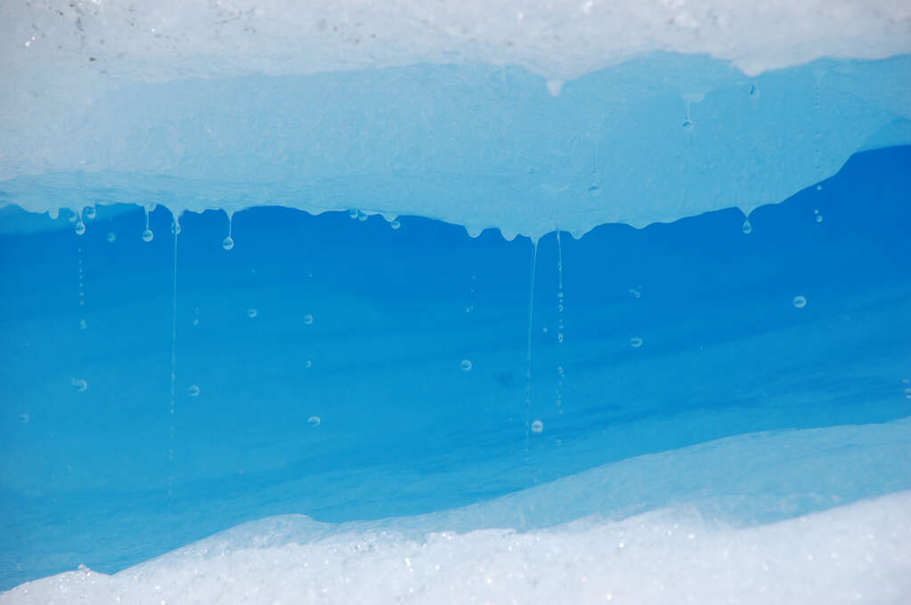 A close-up of water dripping from ice with a blue glow in the background.