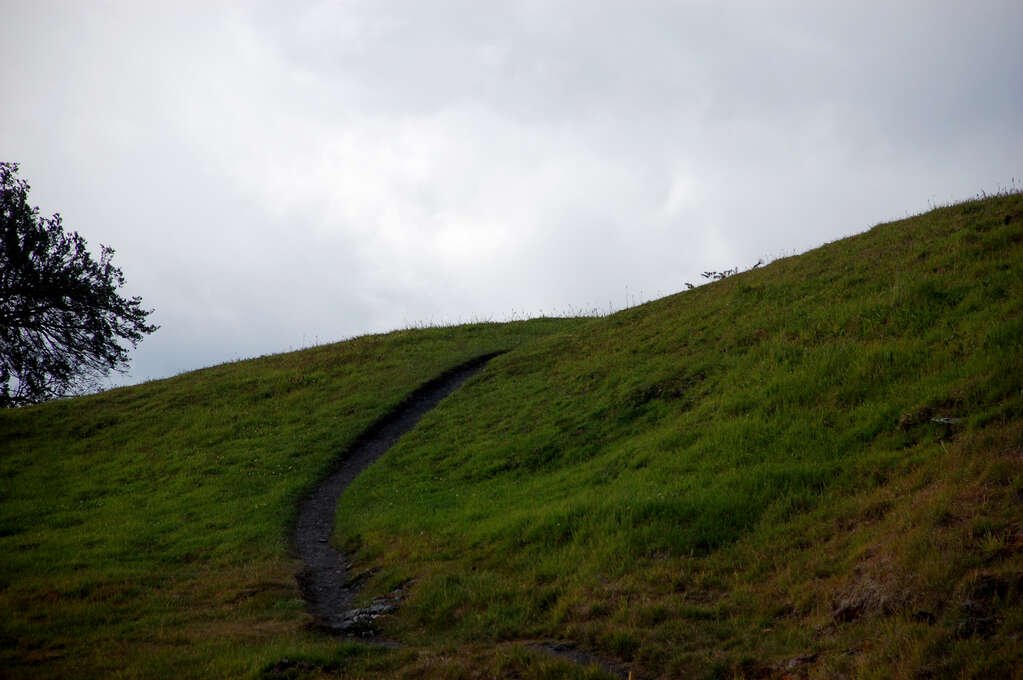 A path leading over and behind a grassy hill.