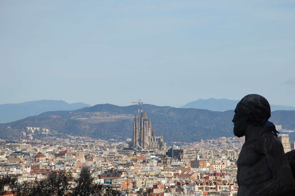 A statue of a man looking out over the city with a large cathedral towering above everything.