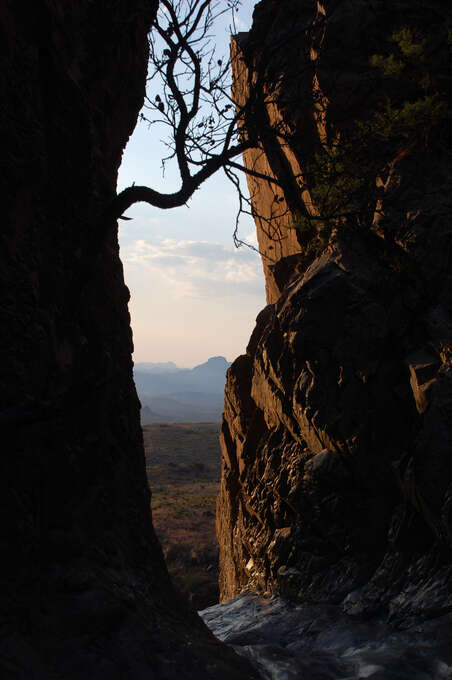 A narrow opening between two large rocks overlooking the ground below.