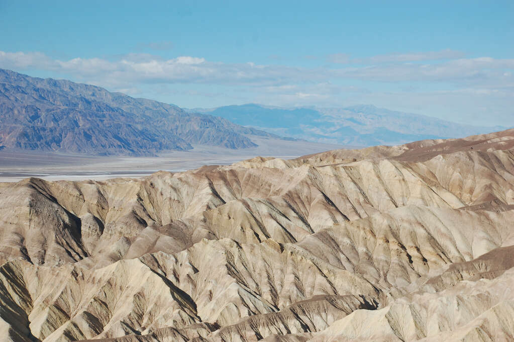 A wide view of many wavy rocks in the foreground with desert and mountains in the background.