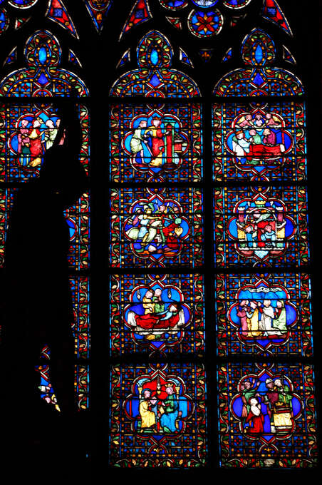 Light coming through colorful stained glass behind the black silhouette of a statue.