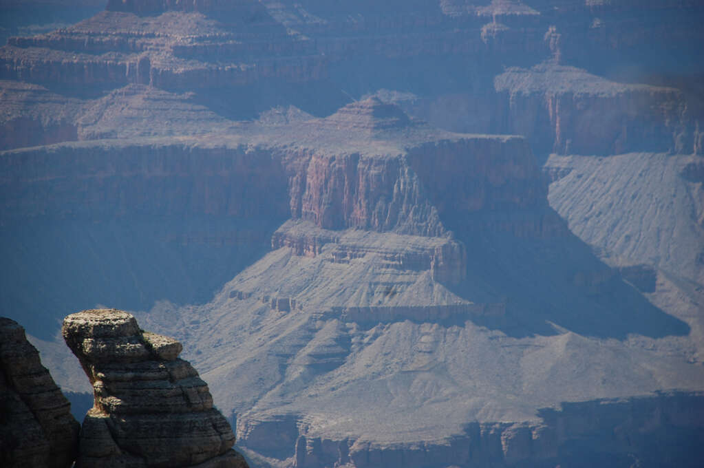 A very large canyon wall in the far background with a small rocky formation in the foreground.