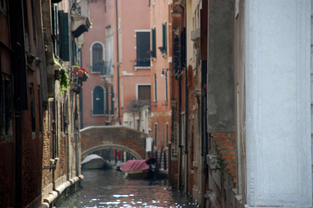 A narrow canal lined with buildings and a bridge in the distance.