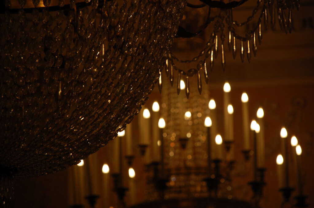 A lit chandelier in the background shining on the crystals of one in the foreground.