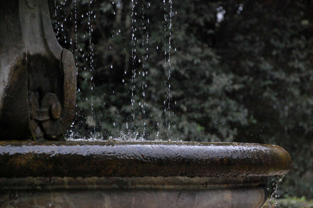 Water droplets dripping into and splashing in a fountain in a garden.