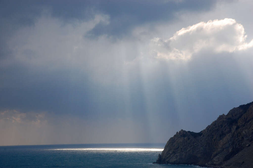 A cloudy sky over the sea with rays of light making a bright spot on the water.