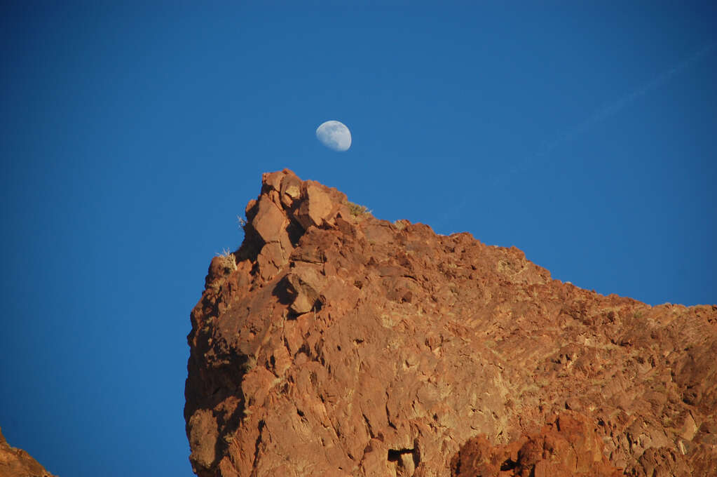 The tip of a rocky outcropping on a hill with the moon just above it.