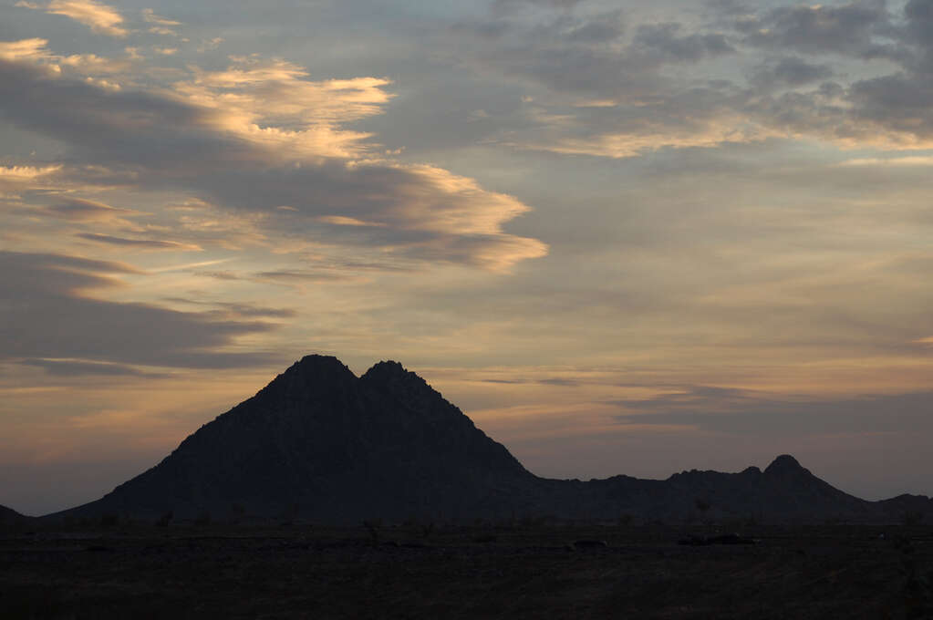 The sun setting behind a double-peaked mountain.