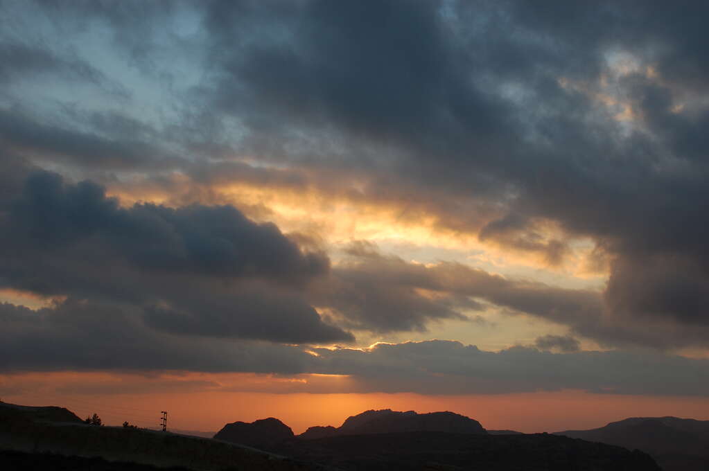 A dark, cloudy sky with bright patches from the setting sun.