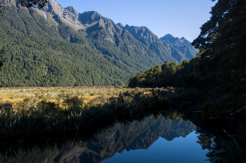 A still lake with a reflection of mountains in the background.