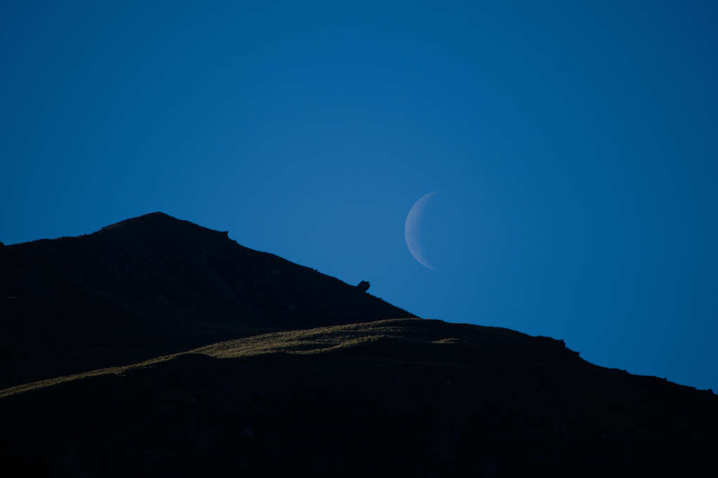 A crescent moon next to a mountain.
