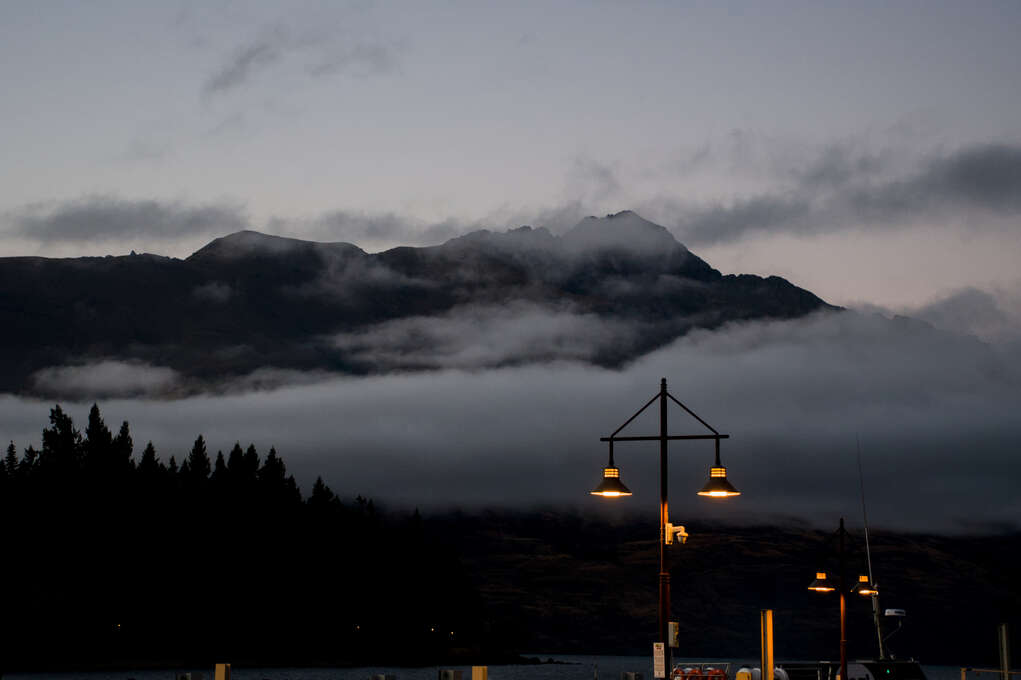 A mountain covered in fog across a lake with lamps on a pier in the foreground.