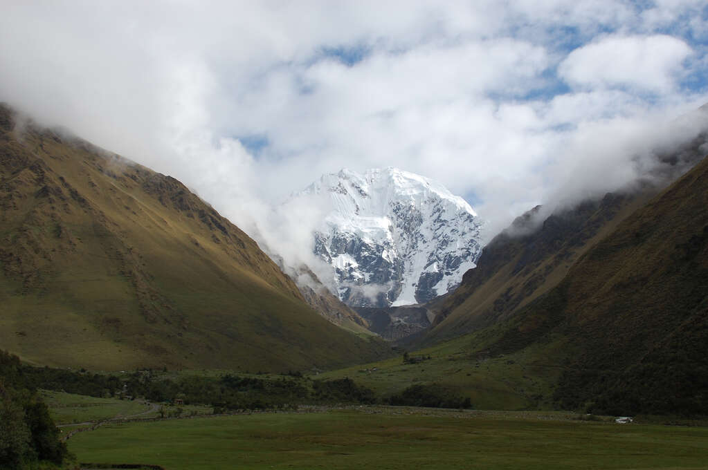 A snow-covered mountain in the distance in the valley between green hills. 