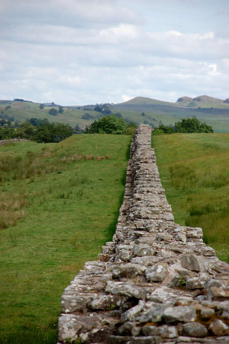 A knee-high stone wall leading directly away from the camera over a small grassy hill.