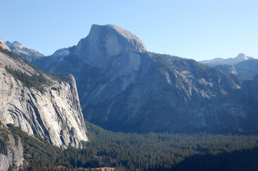 A large rocky mountain in the distance with a curved slope and many dense trees in the valley below.